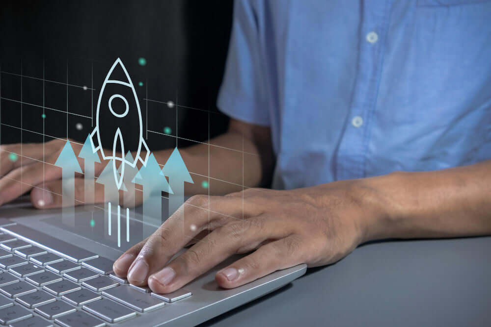 Person typing on a laptop with a graphic of a rocket launch and arrows pointing upwards.